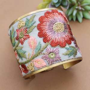 Gold-tone cuff bracelet with white fabric and embroidered pink, orange and green flowers.